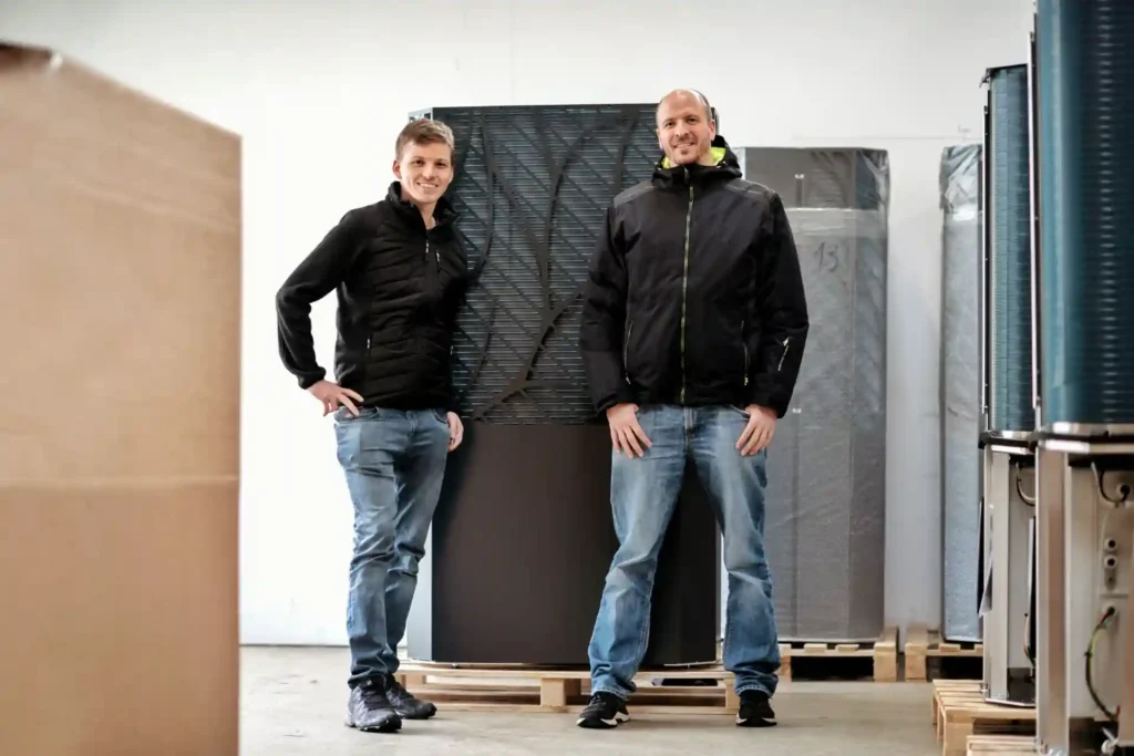 Zwei Männer in Arbeitskleidung stehen vor industriellen Geräten in einer Lagerhalle.
